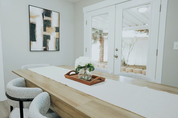 A modern dining area with a wooden table, white chairs, and a vase with white flowers.