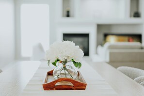 Un plateau en bois blanc sur lequel repose un vase en verre contenant des fleurs blanches, le tout posé sur une table blanche dans un salon moderne.