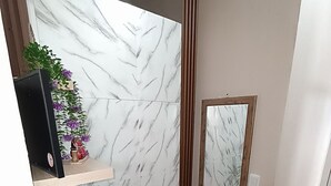 Habitación de esquina con pared con diseño de mármol, repisa de madera con una computadora portátil, planta en maceta y un espejo.