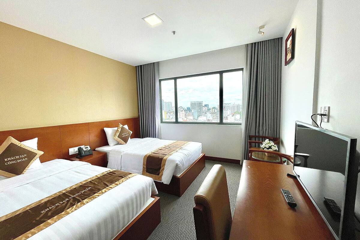 Une chambre d’hôtel avec deux lits, un bureau, une télévision et une vue sur la ville.