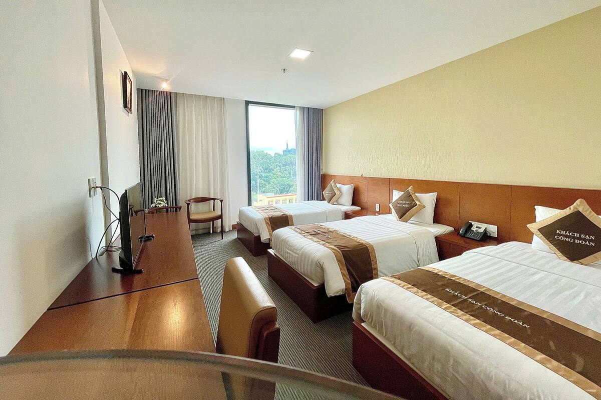 Une chambre d’hôtel avec deux lits, un bureau, une chaise et une grande fenêtre donnant sur la ville.