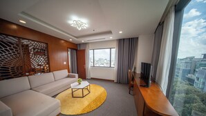 Ein modernes Hotelzimmer mit einer Couch, einem Couchtisch, einem Fernseher auf einem Holzboden und einem großen Fenster mit Blick auf die Stadt.