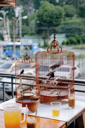Two birdcages with birds, a mug of iced tea, and a glass of iced coffee on a table. - NHA KHACH TONG LIEN DOAN (PHUONG BEN THANH)