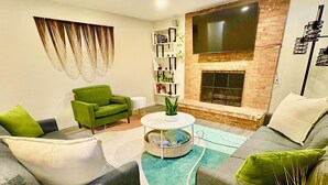 A modern living room with a fireplace, green armchairs, a coffee table, and a flat-screen TV mounted on the wall.