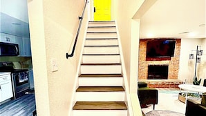 A staircase leading to a bright yellow door, a kitchen with modern appliances, and a living area with a fireplace and seating.