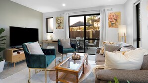 A modern living room with a flat-screen TV, comfortable seating, a glass coffee table, and a view of the outdoors. - Apartment on Short (Christchurch)