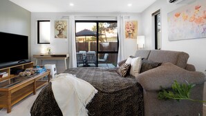 A modern living room with a large flat-screen TV, a sofa, a coffee table, and a dining area with chairs and a table. - Apartment on Short (Christchurch)