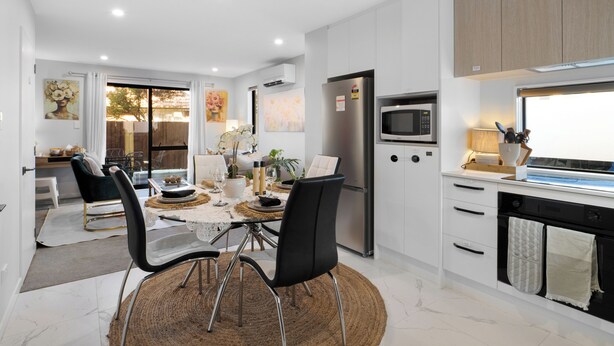 A modern kitchen with white cabinetry, a stainless steel refrigerator, a built-in microwave, and a dining area with a round table and chairs. - Apartment on Short (Christchurch)