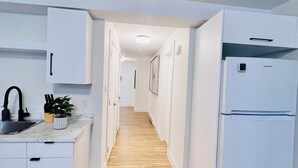 Una cocina estrecha con armarios blancos, un lavamanos y un refrigerador.