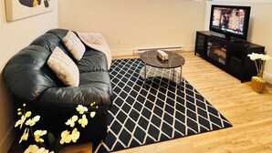 Una sala de estar con un sofá de cuero negro, una mesa de centro, un televisor de pantalla plana y una alfombra estampada.