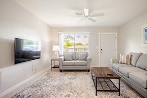A living room with a flat-screen TV, a sofa, a coffee table, and a ceiling fan.