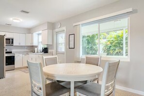 A modern kitchen with white cabinets, a dining table with chairs, and a large window with a view of greenery.