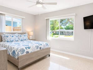 A bedroom with a bed, a ceiling fan, a window, and a TV mounted on the wall.