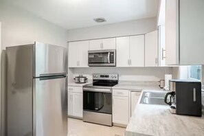 A modern kitchen with stainless steel appliances, white cabinetry, and a marble countertop.