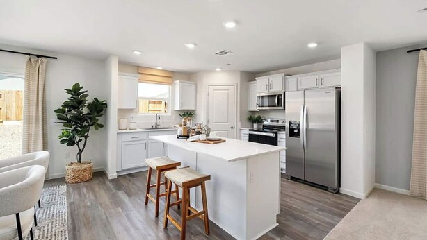 A modern kitchen with white cabinetry, a central island with stools, stainless steel appliances, and a large window with curtains. - Large new construction 3-bedroom near Hospital Hub (Bakersfield)