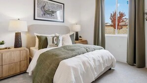 A bedroom with a bed, two bedside tables, a nightstand, a framed picture, and a window with curtains. - Large new construction 3-bedroom near Hospital Hub (Bakersfield)