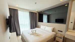 A hotel room with a large bed, a bedside table, a mirror, and a TV mounted on the wall. - 1BR Condo Near Beach with Pool Gym C235 (Choeng Thale)
