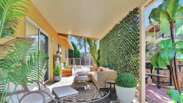 Un espace extérieur ensoleillé, aménagé avec des meubles en osier, un grand tapis à motifs et une grande plante en pot.