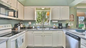 Une cuisine avec des meubles blancs, un four à micro-ondes encastré, une cuisinière, un évier et un lave-vaisselle.