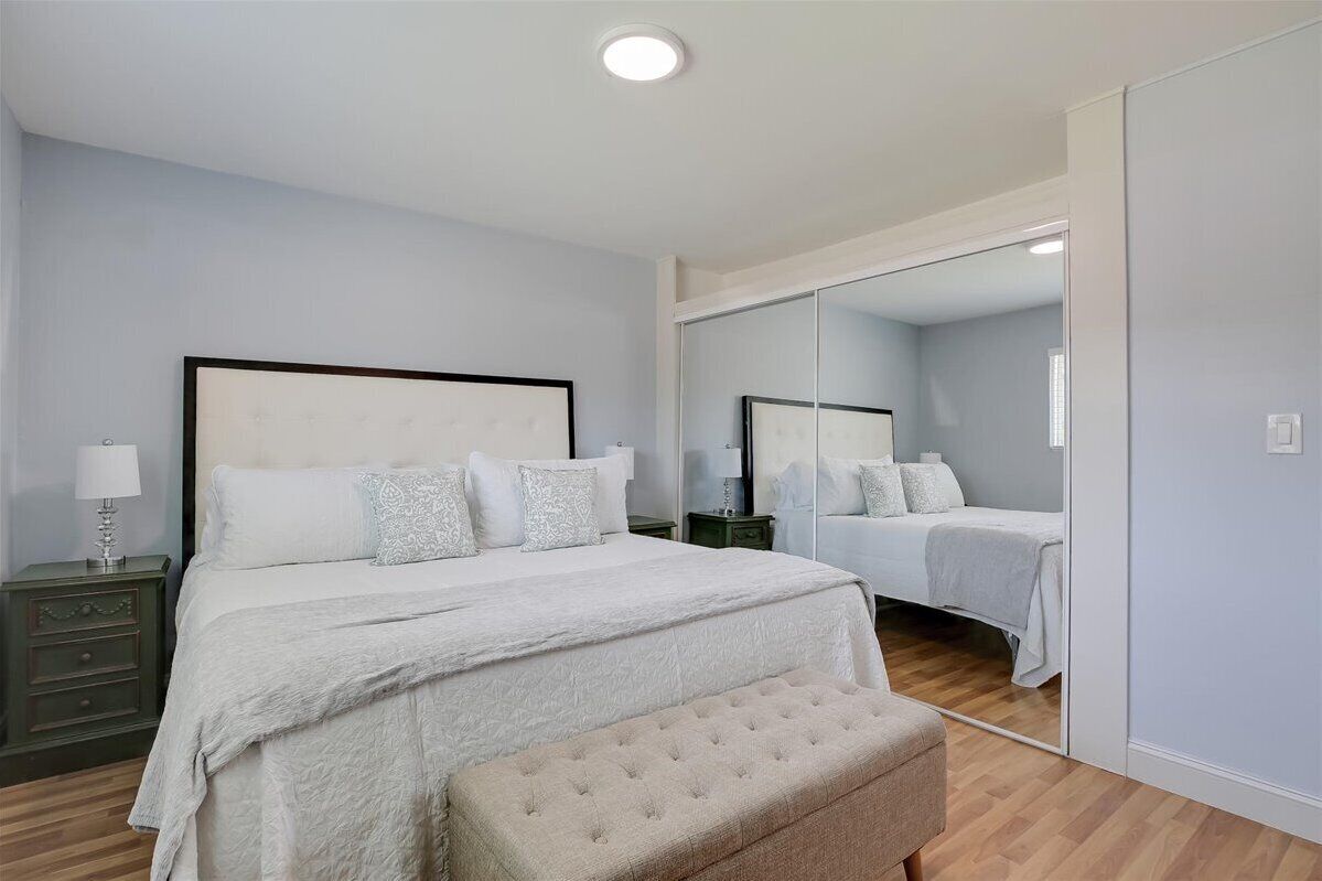 Een slaapkamer met een groot bed, een nachtkastje, een bankje en een spiegel.
