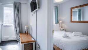 Hotellihuone, jossa on sänky, yöpöytä, lamppu ja seinälle asennettu televisio.
