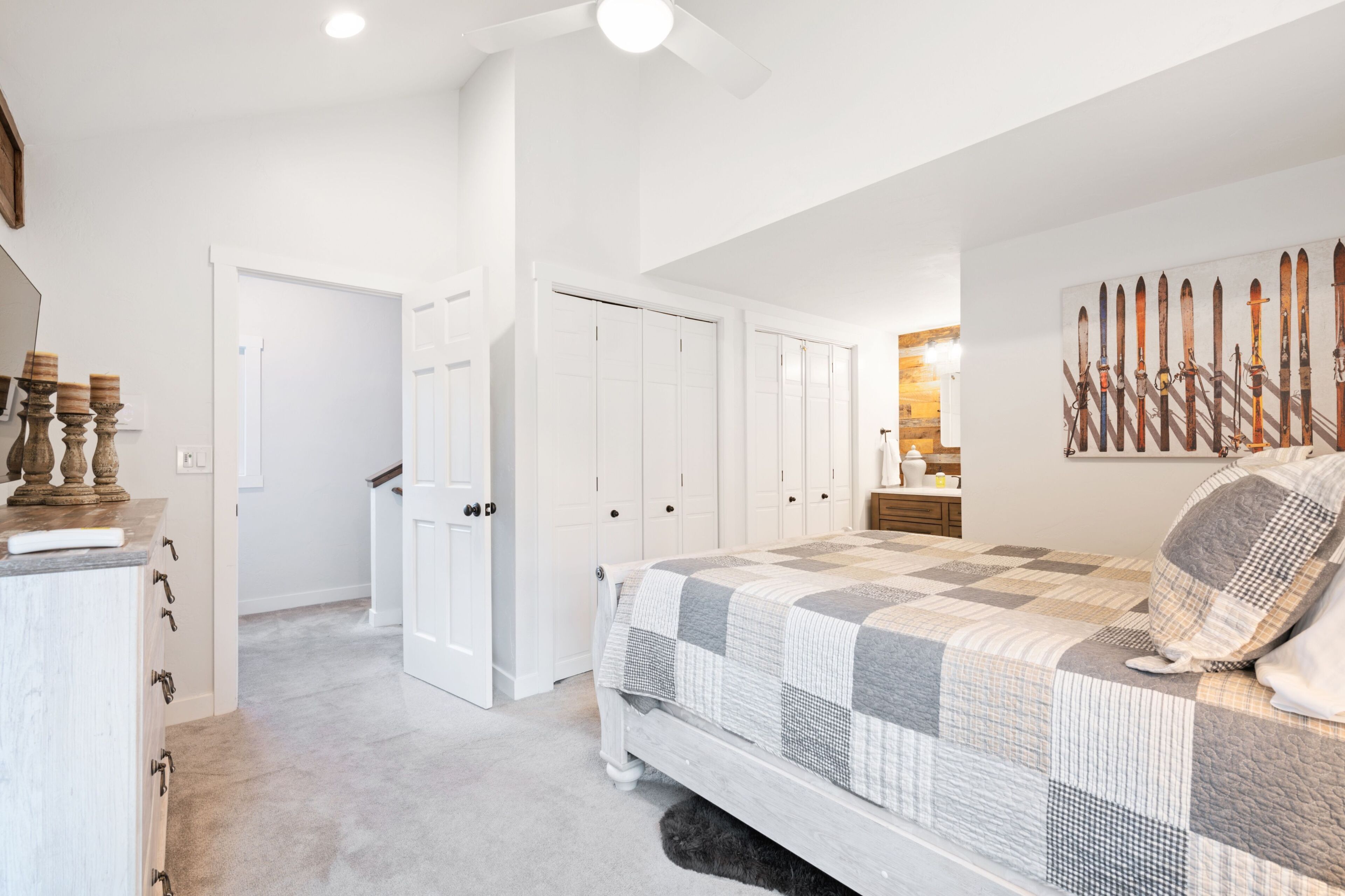 A bedroom with a large bed, a ceiling fan, and a wall-mounted ski rack.