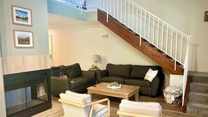 Una sala de estar con chimenea, un conjunto de sofás, una mesa de centro y una escalera.
