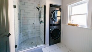 A compact bathroom with a glass shower enclosure, a stacked washer and dryer, and a window providing natural light. - Welcoming updated modern 3-bedroom house in Mount Clemens (Mount Clemens)