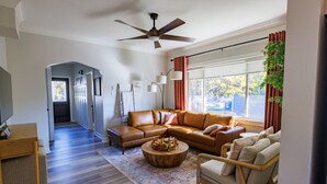 A spacious living room with a large sectional sofa, a coffee table, and a floor lamp. A ceiling fan and a window with curtains are visible. - Welcoming updated modern 3-bedroom house in Mount Clemens (Mount Clemens)