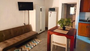 A living room with a sofa, a TV mounted on the wall, a small table with a chair, and a kitchen area visible through an open door. - Sol Caribe Primavera Pool (Punta Cana)