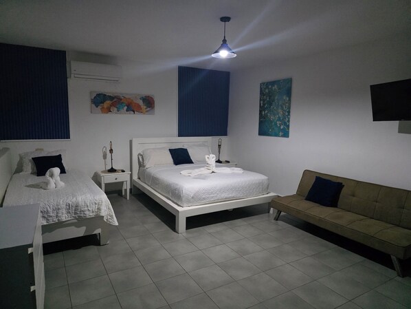 Une chambre avec deux lits, un canapé, un ventilateur de plafond et des œuvres d’art accrochées aux murs.