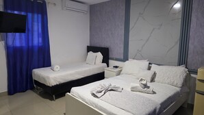 A hotel room with two single beds, a large bed, a flat-screen TV, an air conditioning unit, and a marble-patterned wall. - Sol Caribe Primavera Pool (Punta Cana)