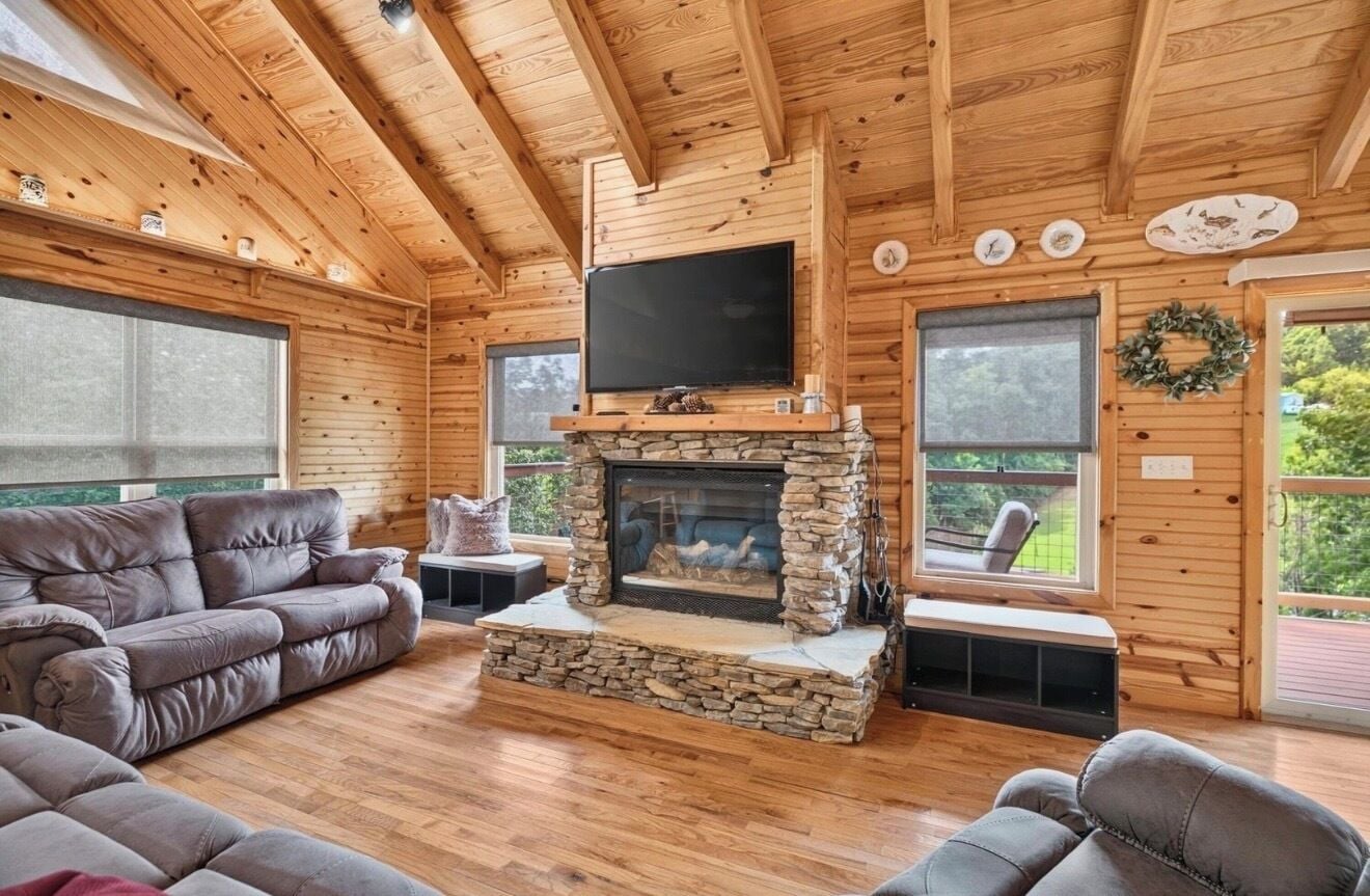 A log cabin interior with a stone fireplace, wooden walls, and a flat-screen TV mounted above it.