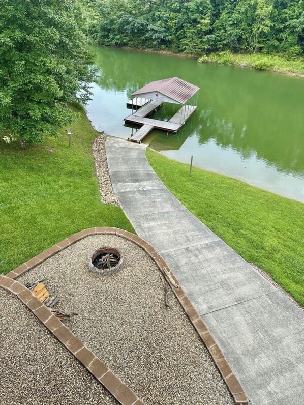 A concrete pathway leading to a dock over a calm lake, surrounded by lush greenery. - Lakefront covered dock sleeps 12 (Dandridge)