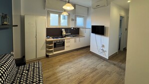 Een compacte keuken met een fornuis, oven en spoelbak, een flatscreen televisie aan de muur bevestigd, en een houten vloer.