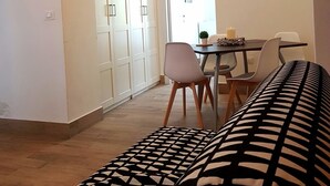 Een moderne woonkamer met een gestreept bankje, een eethoek met een tafel en stoelen, en een grote kledingkast.