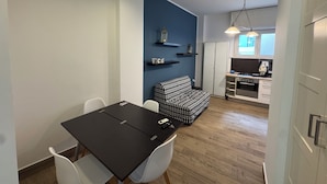 Een knus woongedeelte met een eettafel, witte stoelen, een gestreept bankje, een kitchenette en een blauwe accentmuur.
