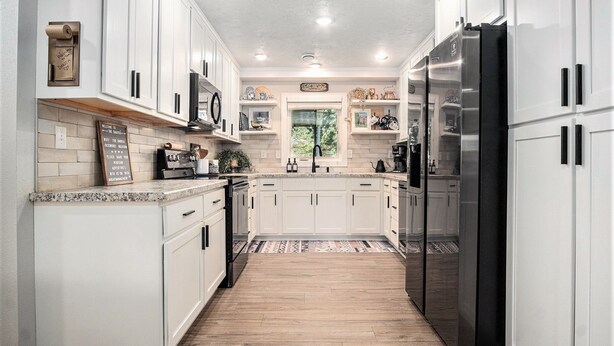 Una cocina moderna con armarios blancos, un refrigerador de acero inoxidable y piso de madera.
