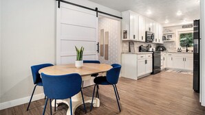 Una cocina moderna con armarios blancos, un refrigerador negro y una mesa de comedor de madera con sillas azules.