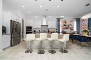 A modern kitchen with stainless steel appliances, a central island with bar stools, and a dining area with a blue tablecloth.
