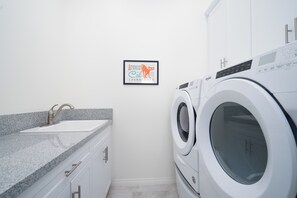 Uma lavanderia com máquina de lavar, pia e um quadro na parede.