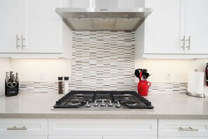 Une cuisine moderne avec des armoires blanches, une hotte en acier inoxydable, un dosseret carrelé et une cuisinière à gaz.