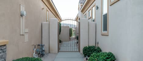 A gated pathway leading to a building with a beige exterior and a stone wall on one side.