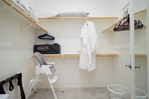 Um closet espaçoso com uma estante de madeira, um roupão branco, um bebê conforto Graco e uma cesta de roupa branca.