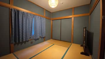 A room with tatami flooring, a ceiling light fixture, a television, and a sliding door.