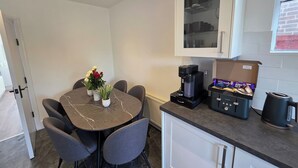 Une cuisine compacte avec une table à manger au plateau en marbre, des chaises grises, une machine à café et une boîte de lait.