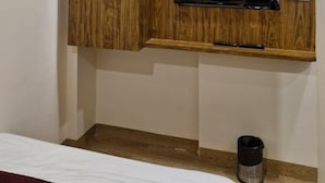 A room with a wooden cabinet, a television mounted on the wall, and a trash bin. - Hotel AL-HAMD (Mumbai)