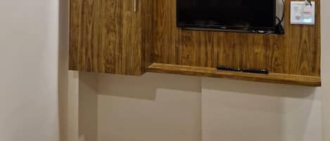 Ein Zimmer mit einem Holzkasten, einem an der Wand befestigten Fernseher und einem Mülleimer.