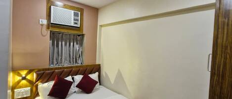 Habitación de hotel con cama, mesita de noche con lámpara, ventilador de techo, aire acondicionado y armario.