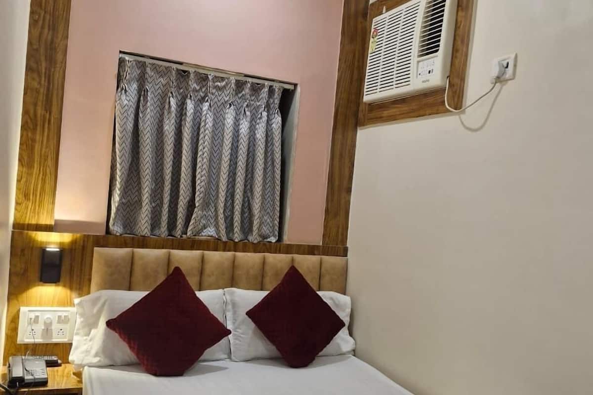 Una cama bien hecha con una colcha roja, un cabecero de madera y una ventana con cortina estampada.